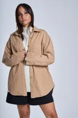 Sobrecamisa color beige confeccionada en gabardina, de corte holgado, con cuello camisero, cierre frontal con botones, dos bolsillos de parche en el pecho y mangas largas con puños abotonados.