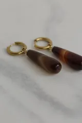 Aros colgantes de acero dorado hipoalergénico con dije en forma de gota de piedra natural con patrón salpicado.