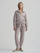 Campera deportiva con cierre frontal, cuello alto tipo chimenea y mangas raglán. Es de corte holgado y presenta bolsillos de parche delanteros. El color es un tono neutro entre gris y rosado (taupe).