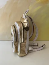 Mochila Lucy de cuero blanco y detalles dorados, con diseño de arte pintado a mano en el bolsillo frontal, cierre superior y correas ajustables.