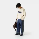 Sweater de punto color crema con finas rayas horizontales en beige. Presenta un logo grande con la palabra "EME" en azul marino en el frente y tiene cuello redondo y corte holgado.