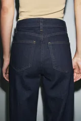 Jeans de tiro alto estilo wide leg, color marrón oscuro, con diseño de cinco bolsillos y cierre frontal de cremallera y botón metálico.