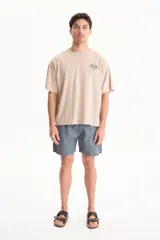 Remera beige de manga corta y corte oversize, con estampa en la espalda con temática de tenis y texto descriptivo.