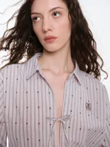 Camisa de dormir de popelina de algodón, con estampado de rayas verticales y pequeños motivos geométricos. Presenta cuello camisero, mangas largas y cierre frontal mediante lazos ajustables.