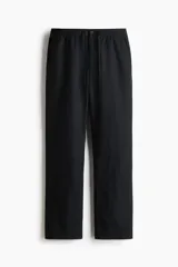 Pantalón negro de corte regular, confeccionado en una mezcla vaporosa de lino y algodón. Presenta cintura con elástico revestido y cordón de ajuste, cierre con botón y bragueta, bolsillos laterales y bolsillos traseros insertados.