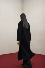 Abrigo largo de lana reciclada en color negro, con cuello redondo, cierre frontal con botones ocultos, bolsillos laterales y aberturas en los costados.