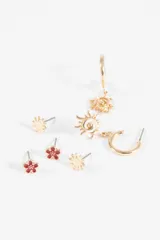 Set de tres pares de aros de metal plateado. Incluye un par de aros tipo stud con forma de flor con centro esmaltado en rojo, un par de aros tipo stud con forma de sol pequeño y un par de aros tipo argolla con dije colgante en forma de sol con diseño espiral.