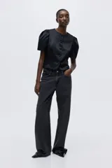 Blusa corta de sarga negra con leve brillo, ajuste entallado, escote redondo, botones forrados al frente y mangas cortas abullonadas con pliegues. Presenta costuras princesa al frente para estilizar la silueta.