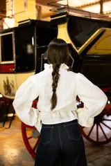 Camisa de lino color negro con cuello alto, volados frontales y mangas largas abullonadas con puños elásticos. Presenta cierre frontal con botones ocultos.