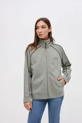 Campera de felpa con friza, color verde oliva, con cierre metálico frontal, cuello alto y detalles de vivos en color bordó. Presenta un bordado en el pecho y corte relaxed.