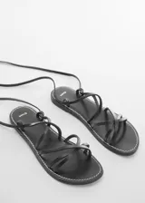 Sandalia plana negra de cuero con tiras finas que se atan al tobillo.