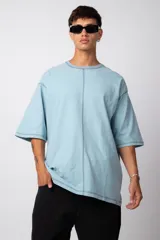 Remera de corte oversize color malva, confeccionada en algodón pesado, con costuras externas visibles en color blanco que recorren el centro, el cuello y los bordes de las mangas.