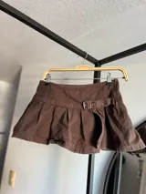 Minifalda de tiro bajo confeccionada en denim negro, con diseño plisado y detalle de hebilla frontal. Presenta un tajo lateral que aporta un estilo moderno y audaz.