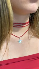 Gargantilla tipo choker compuesta por tres tiras finas de gamuza roja y un collar largo con dije de estrella plateada.