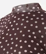 Blusa de manga larga ajustada al cuerpo, confeccionada en tul marrón con estampado de lunares blancos. Presenta cuello redondo y un cárdigan negro cruzado sobre los hombros.