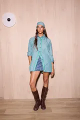 Camisa holgada de algodón con rayas verticales en tonos verde agua, rosa pálido y blanco. Presenta una abertura frontal que llega hasta la mitad del torso, ribeteada con un cordón ondulado de color verde brillante. Incluye botones oscuros y un pañuelo a juego en la cabeza.