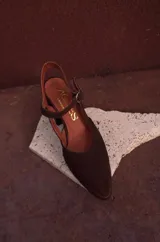 Sandalia de gamuza color marrón, con taco ancho, punta fina y tira ajustable al tobillo. Incluye detalle metálico en la puntera.