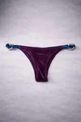 Bottom de bikini de terciopelo color morado, con tiras laterales en tono azul y detalles de estribos metálicos argollas en los laterales.