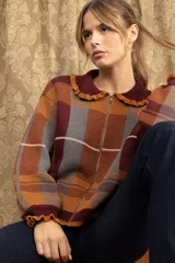 Campera de punto con diseño a cuadros tartán en tonos marrones y beige. Presenta un corte oversize, cierre frontal con cremallera, cuello tipo babero con volados y mangas largas con puños ajustados.