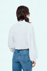Camisa blanca de manga larga abullonada, con cuello alto y volados delicados en el borde.