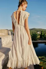 Vestido largo color crudo, sin mangas, con escote en V pronunciado, canesú superior de tejido de punto con botones frontales y lazo para atar en el cuello, y falda fluida con detalle de bordado en el bajo.