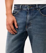 Pantalón de jean corte slim color azul claro con efecto de lavado desgastado. Cuenta con cierre frontal con botón, pasadores para cinturón y bolsillos funcionales.