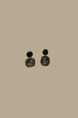 Aros colgantes compuestos por dos piezas de cristal facetado en tonos oscuros, con engaste de borde dorado texturizado.