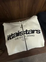 Buzo con cierre frontal completo, capucha amplia y bolsillos tipo canguro. Presenta estampado gráfico en el pecho con la marca IttaiStars y diseño de corte holgado.
