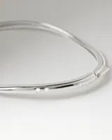 Brazalete rígido plateado de la marca PDPAOLA, modelo Aire, con diseño sutilmente ondulado e incrustaciones de circons en la parte superior.