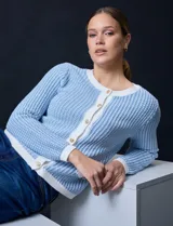 Cardigan de tejido tweed celeste y blanco, con escote redondo, cierre frontal con botones metálicos dorados y bolsillos simulados en el frente.