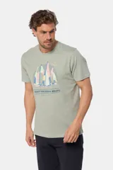 Remera de manga corta color verde grisáceo con cuello redondo. Presenta un estampado frontal de veleros sobre un fondo circular con líneas verticales, y texto bordado debajo.