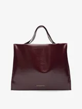 Maxi shopper de diseño minimalista con acabado brillante y textura craquelada. Cuenta con un compartimento principal con cierre magnético, bolsillo interior con cremallera y asas de hombro integradas. Logo de la marca grabado en la parte inferior frontal.