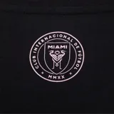 Remera blanca de manga corta con cuello redondo. Estampado frontal con la palabra "Miami" en cursiva sobre el escudo del Inter de Miami.