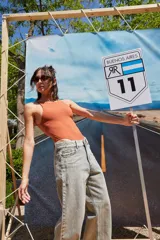 Body color marrón oscuro, confeccionado en microfibra, con escote delantero y trasero cerrado, cuerpo embolsado y gancho corsetero regulable en la entrepierna.