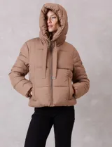Campera puffer de corte recto y acabado mate, con diseño de bloques horizontales acolchados. Presenta capucha integrada con cordones de ajuste, cierre frontal metálico y bolsillos laterales invisibles. Incluye puños elásticos internos para mayor protección contra el frío.