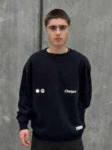 Buzo negro de corte holgado con cuello redondo y puños y bajo acanalados. Estampado frontal con un sol y la palabra "Osten" en blanco.