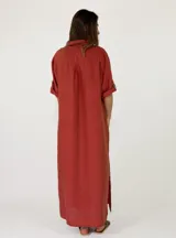 Vestido largo de lino marrón con cierre frontal de botones, cuello camisero, mangas tres cuartos con presilla y costuras decorativas blancas en la botonera.