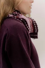 Polera tejida en lambswool color beige, con cuello alto y diseño de intarsia en tonos marrones y grises. Presenta botones forrados en el cuello para modular la apertura.