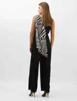 Enterito de seda fría con pantalón palazzo de corte ancho y fluido. Presenta un diseño asimétrico con una tira fina en un hombro y un detalle de herraje metálico en el otro, del cual se desprende una capa de gasa estampada con patrón abstracto en blanco y negro.