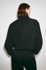 Campera deportiva de sherpa cálida y suave, color negro, con cuello elevado, cierre frontal y bolsillos laterales. Cuenta con corte holgado y elásticos en puños y bajo.