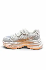 Championes deportivos chunky color blanco con suela gruesa y detalles en tono anaranjado en la parte inferior, con cordones gruesos estilo cuerda.
