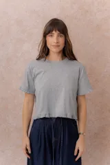 Remera de calce relajado y largo crop, color gris melange, con escote redondo, manga corta y detalles de volados en las mangas y en el ruedo.