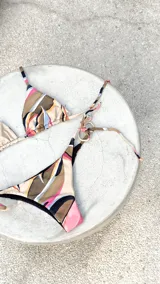 Bikini reversible de diseño triangular con tiras para atar y apliques de argollas metálicas. El conjunto presenta un estampado abstracto multicolor.