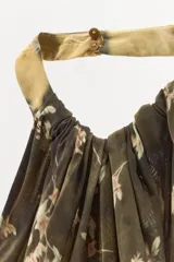 Vestido largo de viscosa con estampado floral y diseño de paneles diagonales en tonos tierra. Presenta cuello halter con cierre de botones y abertura frontal en el pecho, dejando los hombros al descubierto.