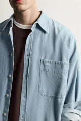 Camisa regular fit de denim de algodón con efecto lavado, cuello solapa y manga larga con puño abotonado. Tiene un bolsillo de parche en el pecho con detalle bordado a contraste y cierre frontal con botonadura.