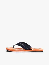 Ojotas Tommy Hilfiger con base naranja estampada con motivos florales blancos y tira de tela azul con logo de la marca.