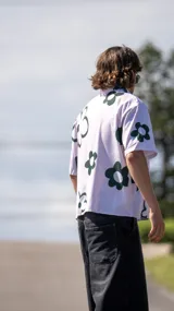 Camisa de manga corta, color blanco, con estampado de flores grandes en verde oscuro. Tiene cuello camisero y cierre frontal de botones.