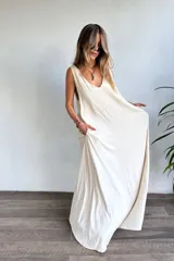 Vestido largo sin mangas, color natural/crudo, con escote en V profundo y corte holgado. Presenta aberturas laterales en la falda.