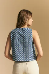 Chaleco corto sin mangas, color azul con estampado geométrico en blanco. Presenta escote en V pronunciado y lazos ajustables en el centro frontal.