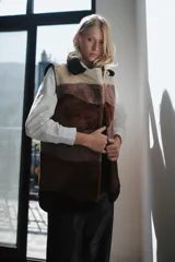 Chaleco largo de piel de oveja con bloques de color en tonos marrón, beige y blanco. Tiene cuello solapa y cierre con un botón forrado en piel.